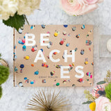 Book titled 'Beaches' by Gray Malin on a decorative surface with flowers and candles.