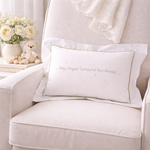 White pillow with embroidered text on a beige armchair with decorative items.
