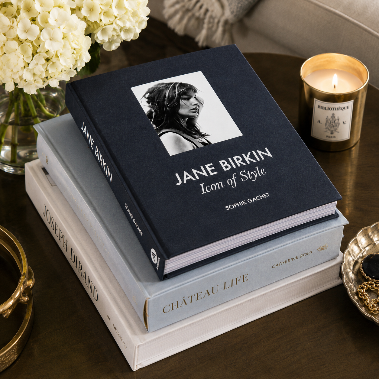 Stack of books on a table with a candle and flowers in the background