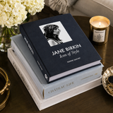 Stack of books on a table with a candle and flowers in the background