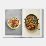 Open cookbook showing two recipes, one in a white dish and the other in a metal pan with a spoon.