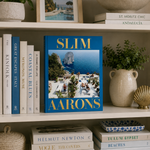 Book titled 'Slim Aarons' on a shelf with other books and decorative items.