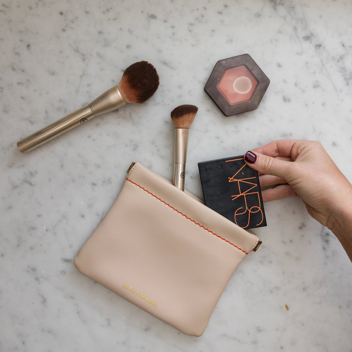 Makeup brushes and a Montemare Roma Square Pouch in Ivory on a marble surface