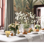 Decorative table setting with flowers and candles in a room with patterned wallpaper.