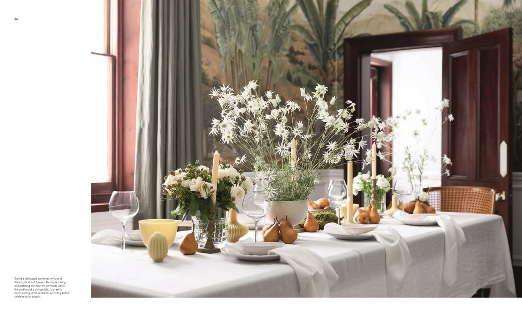 Decorative table setting with flowers and candles in a room with patterned wallpaper.