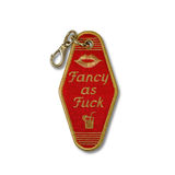 A vintage hotel room key embroidered patch in red with gold trim, featuring the text 'Fancy as Fuck' in gold lettering, a gold lip print, and a small cocktail icon. The patch is attached to a gold metal carabiner clip and shown on a plain white background.