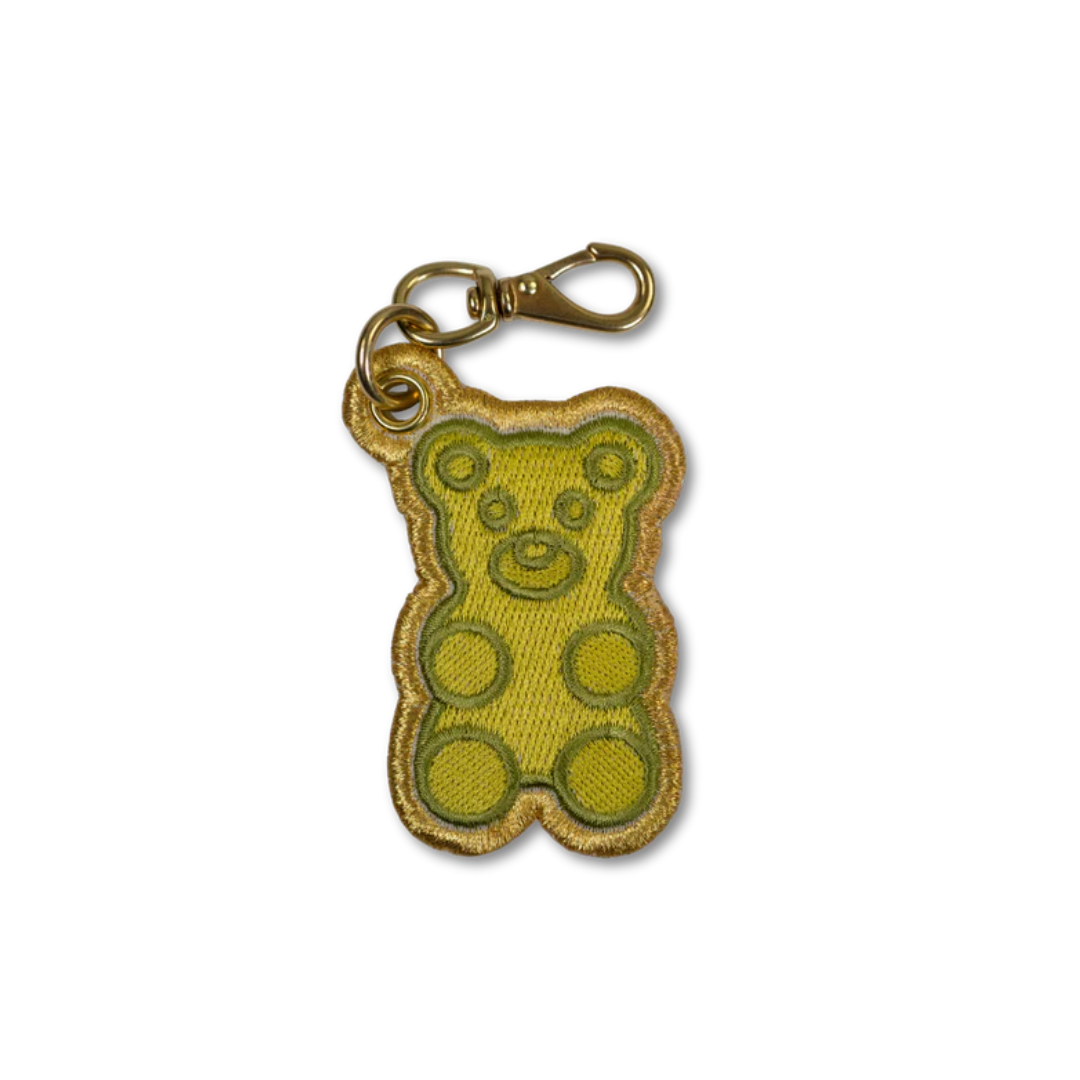 An embroidered gummy bear keychain charm in yellow-green with a gold metallic border and a gold lobster clasp, shown on a plain white background.