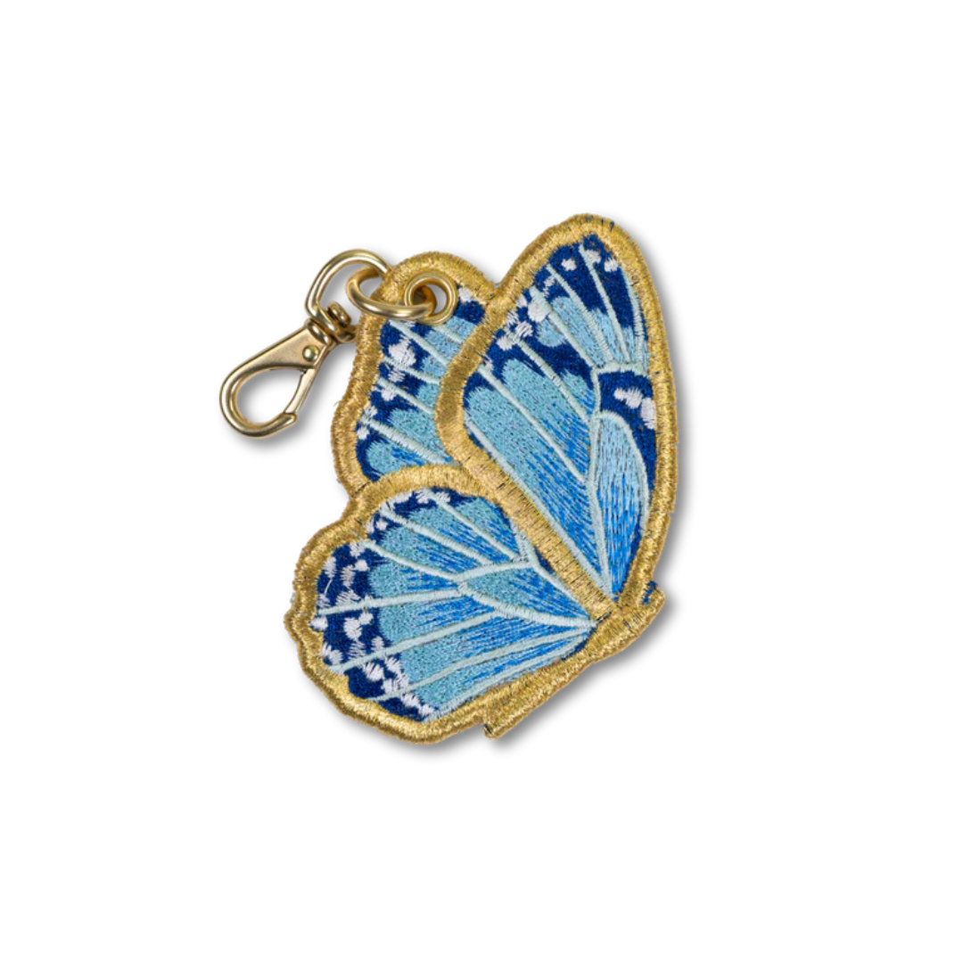 An embroidered butterfly-shaped keycharm with light blue and dark blue stitched wings, outlined in gold thread, attached to a gold lobster clasp, shown on a plain white background.