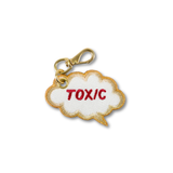 An embroidered cloud-shaped keychain charm with a gold border, white center, and the word 'TOXIC' embroidered in red, attached to a gold lobster clasp on a white background.