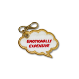 An embroidered speech bubble keychain charm with a gold border, white center, red embroidered text reading 'EMOTIONALLY EXPENSIVE', and a gold lobster clasp on a plain white background.