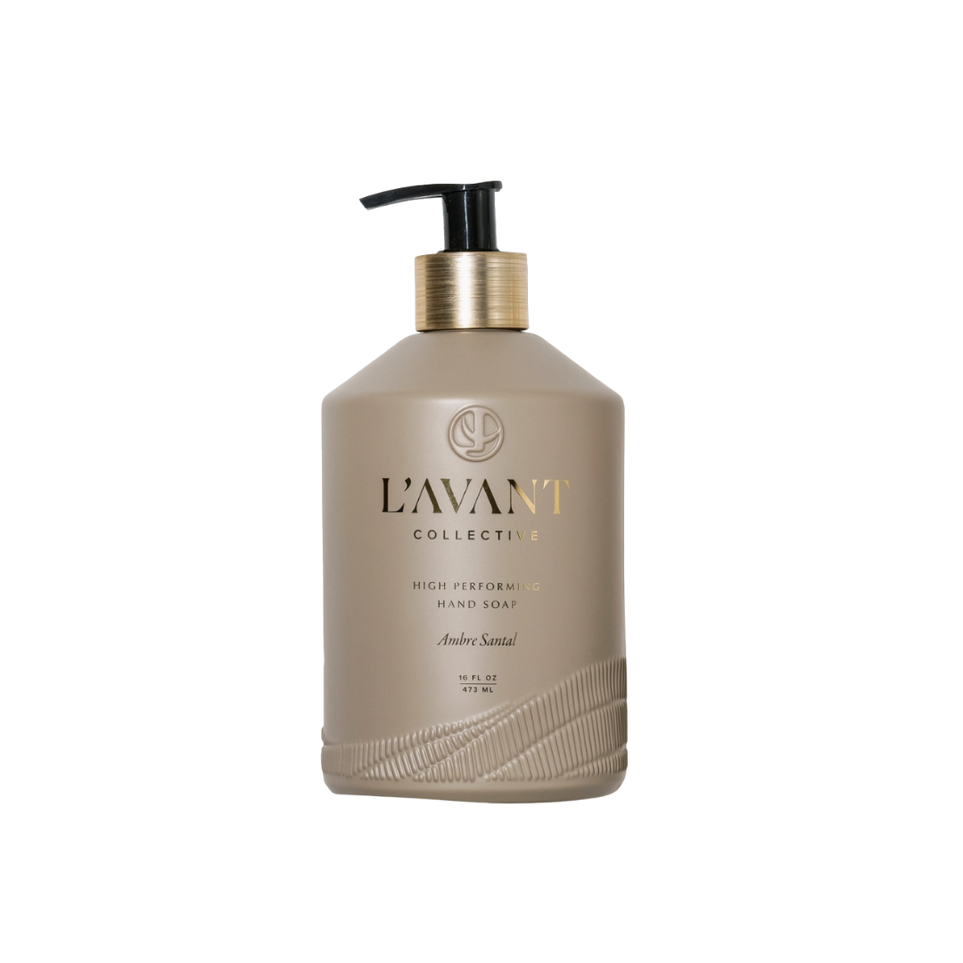A bottle of L'avant Collective hand soap in the Amber Scent variant, featuring a matte taupe-beige bottle with a black pump and gold collar, set against a plain white background.