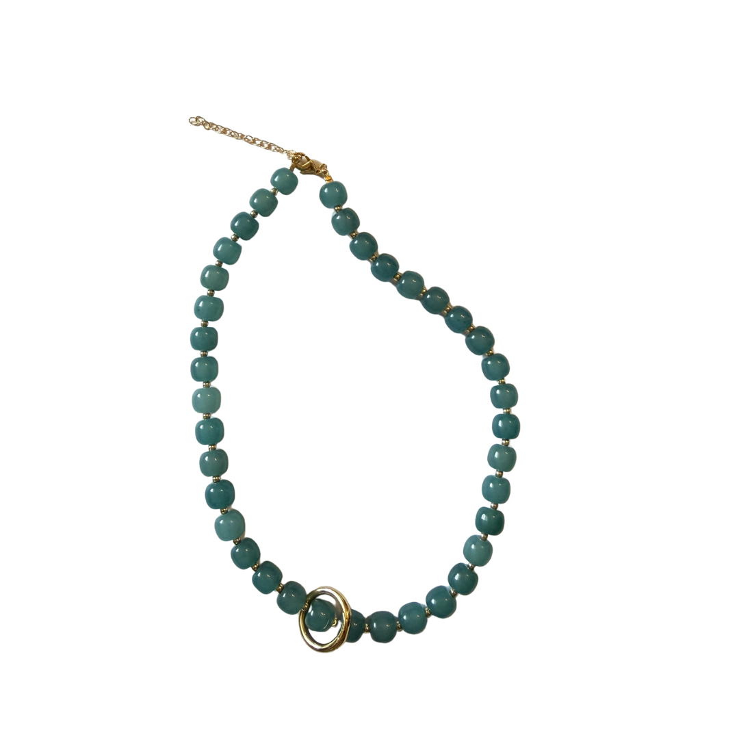A beaded necklace featuring round, polished teal-green beads with a gold-toned double-ring accent and extender chain, displayed on a clean white background.