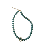 A beaded necklace featuring round, polished teal-green beads with a gold-toned double-ring accent and extender chain, displayed on a clean white background.