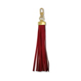 A red faux-leather tassel keychain with gold-tone metal hardware, including a lobster clasp and a rectangular cap, shown on a plain white background.