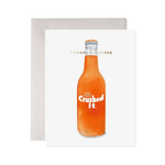 Greeting card with an orange bottle labeled 'Crushed It.' and 'Congratulations' text.