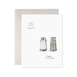 Greeting card with salt and pepper shakers illustration and text 'Still good together, happy anniversary' on a white background.