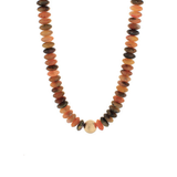 A beaded necklace made of flat, polished oval stones in earthy terracotta, brown, and orange tones, with a single round light beige bead at the center, shown on a plain white background.