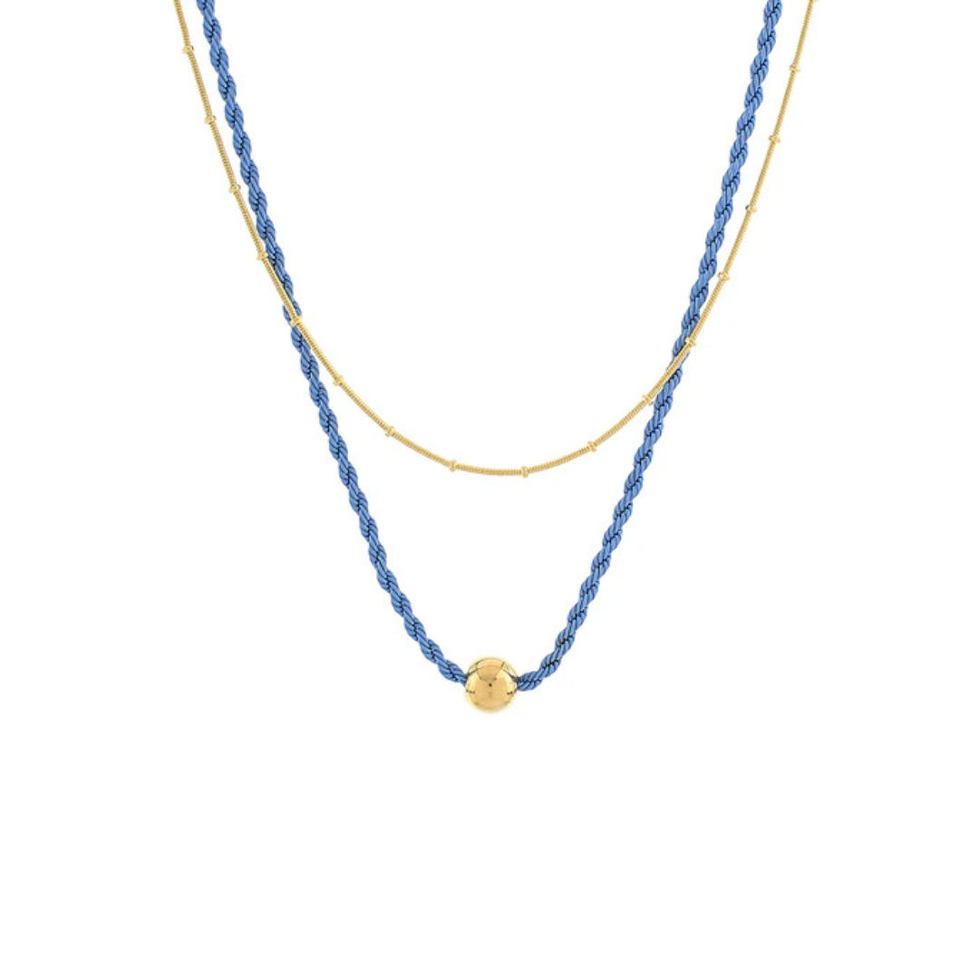 A double-layered necklace featuring a textured blue beaded strand and a fine gold chain, with a small gold bead accent at the center of the blue strand, shown against a plain white background.