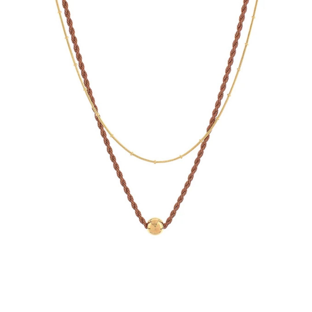 A double-layered necklace featuring a textured brown braided chain with a small gold bead pendant and a delicate gold chain layered underneath, shown against a plain white background.