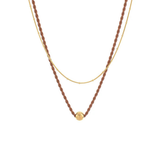 A double-layered necklace featuring a textured brown braided chain with a small gold bead pendant and a delicate gold chain layered underneath, shown against a plain white background.