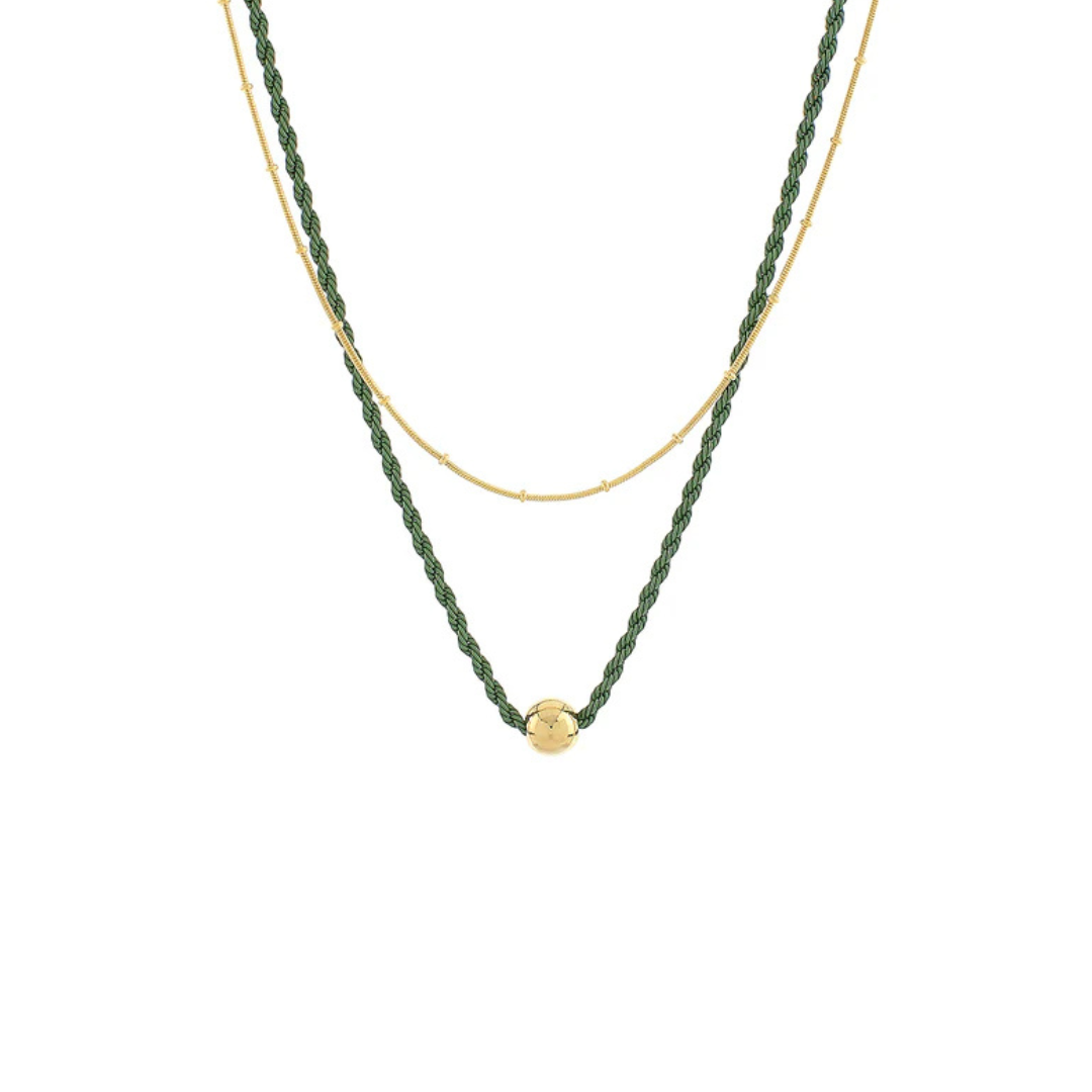 A double-strand necklace featuring a textured dark green beaded strand and a fine gold chain, with a small gold ball pendant at the center, shown against a plain white background.