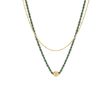 A double-strand necklace featuring a textured dark green beaded strand and a fine gold chain, with a small gold ball pendant at the center, shown against a plain white background.