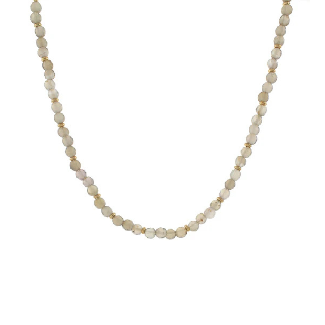 A delicate beaded necklace featuring small, round, pale cream-colored beads separated by tiny gold spacer rings, displayed against a solid white background.