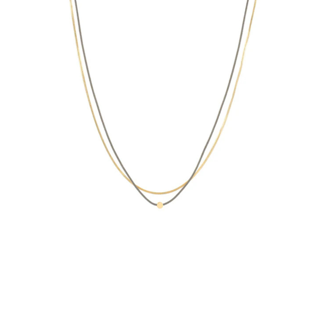 A delicate double-strand necklace featuring one thin gold chain and one thin silver chain, with a tiny gold bead accent at the center of the V-shaped drop, shown against a plain white background.