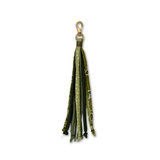A purse tassel accessory featuring multiple fabric strips in shades of olive green, forest green, and dark green, some with white polka dots and others with a subtle pattern, finished with a gold-tone split ring and lobster clasp.