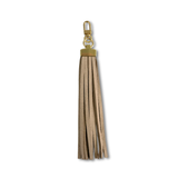 A light tan faux-leather tassel keychain charm with gold-tone metal hardware, shown against a plain white background.