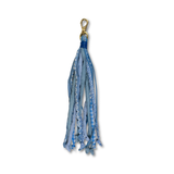 A blue fabric tassel accessory with multiple patterned and solid blue ribbon strands, finished with a gold metal clasp at the top, shown on a plain white background.