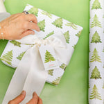 Person wrapping a gift with green tree-patterned paper on a green background