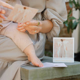 Person sitting on a stone bench with a child, holding a card with an angel illustration.