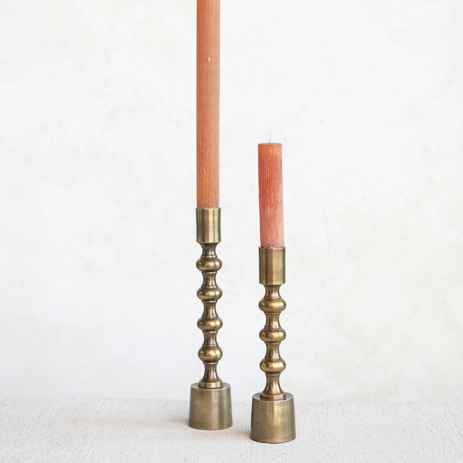 Tall and short Anderson taper holders in antique gold finish styled with blush taper candles on a linen surface.