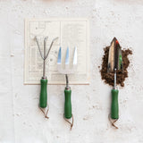 Gardening tools with green handles on a textured white surface.