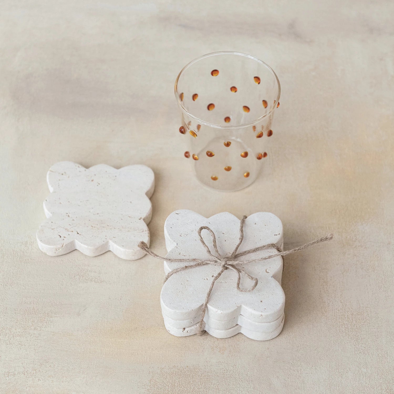 styled set of four travertine scalloped coasters tied together with jute rope with beige background and drinking glass