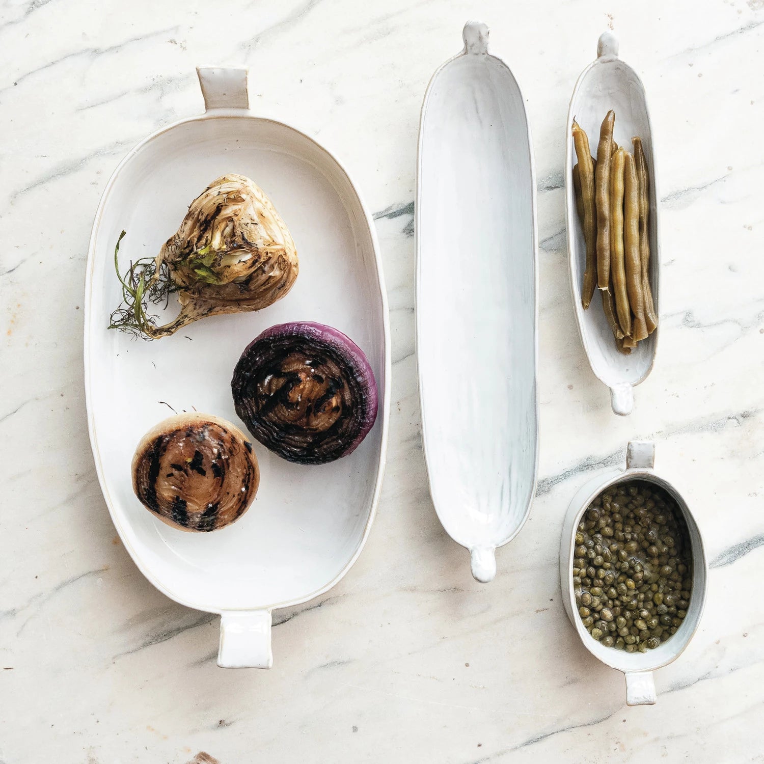 Set of white ceramic dishes with various food items on a marble surface