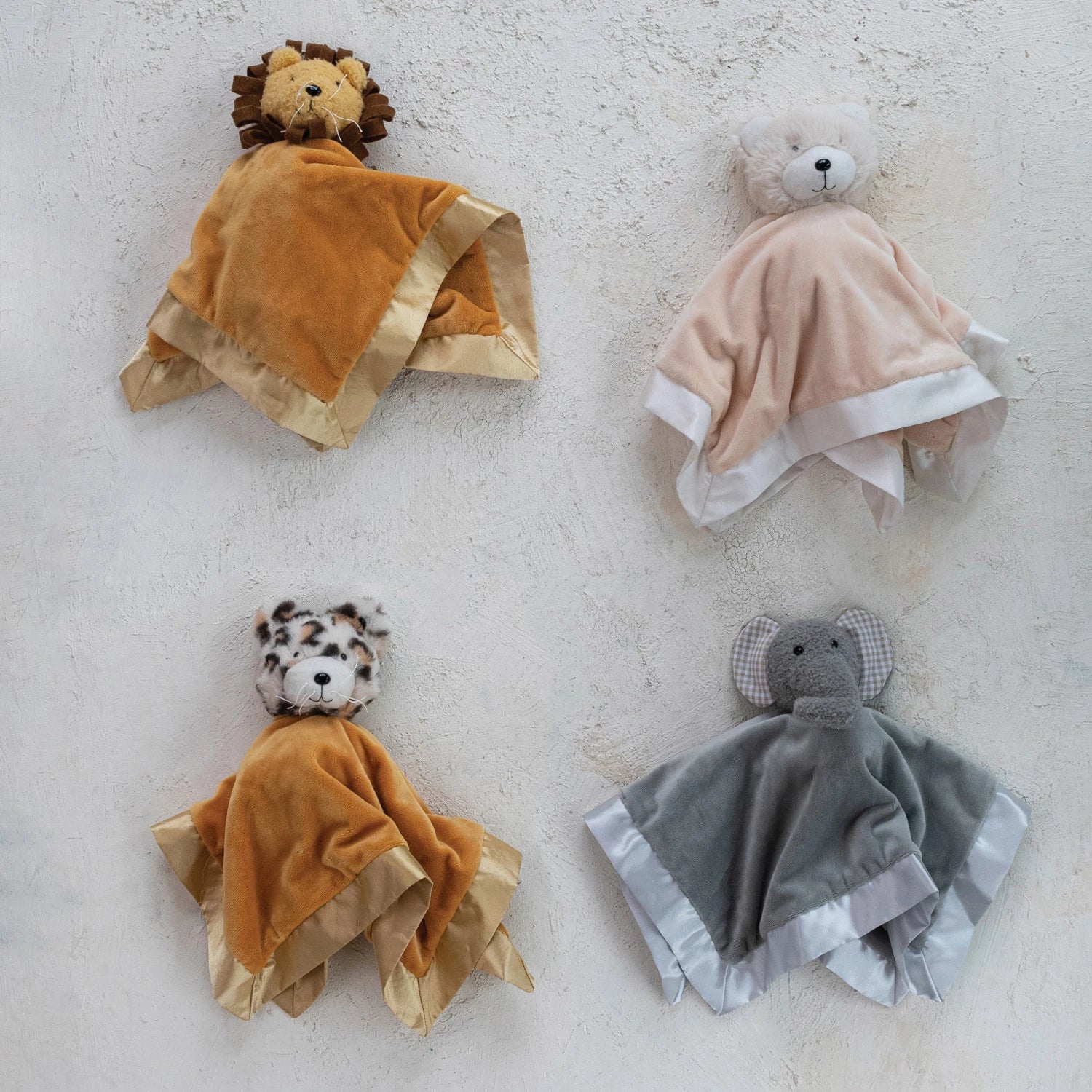 Four soft toy blankets shaped like animals on a textured surface