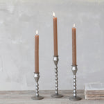 Three brown candles in silver candle holders on a wooden surface with a gray background