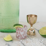 Cocktail with lime wedges and a gold shaker on a marble surface