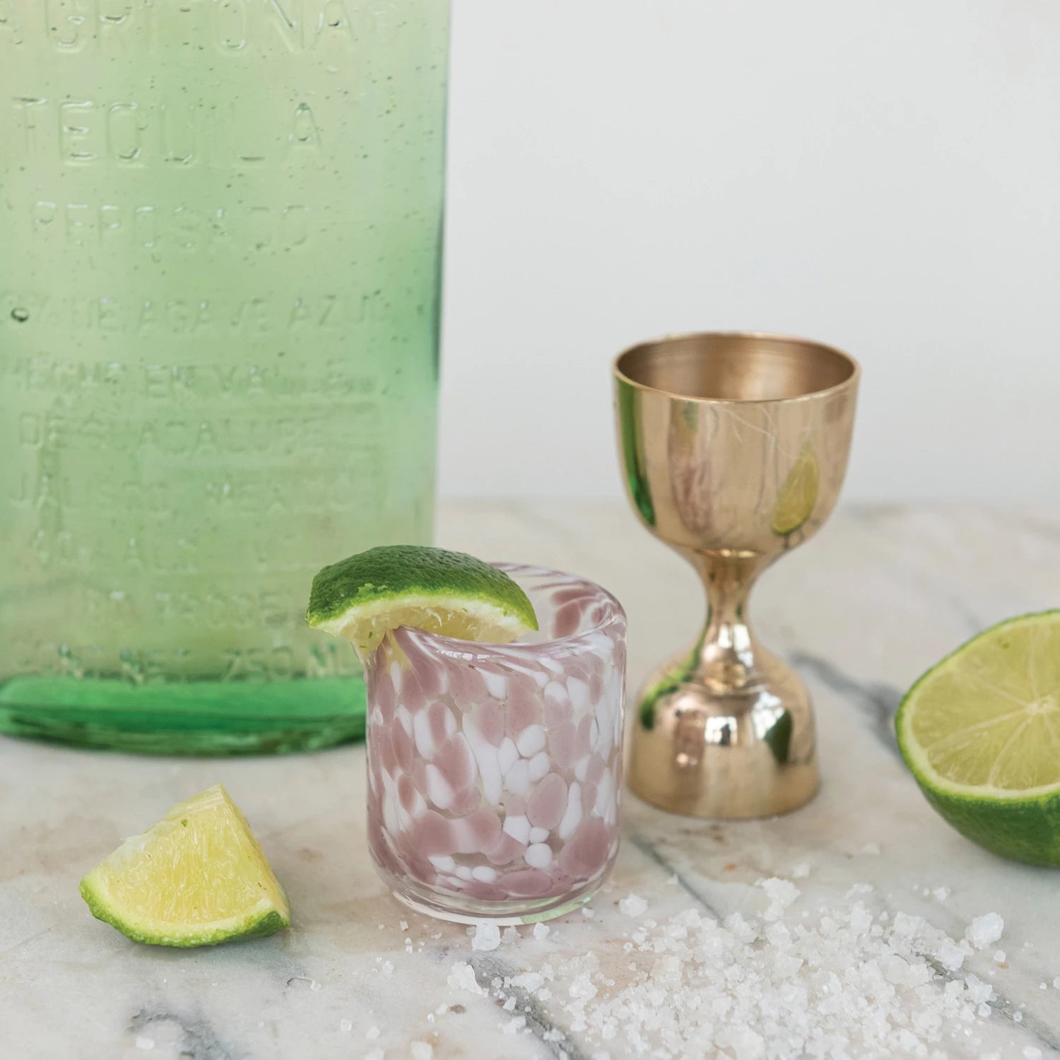 Cocktail with lime wedges and a gold shaker on a marble surface
