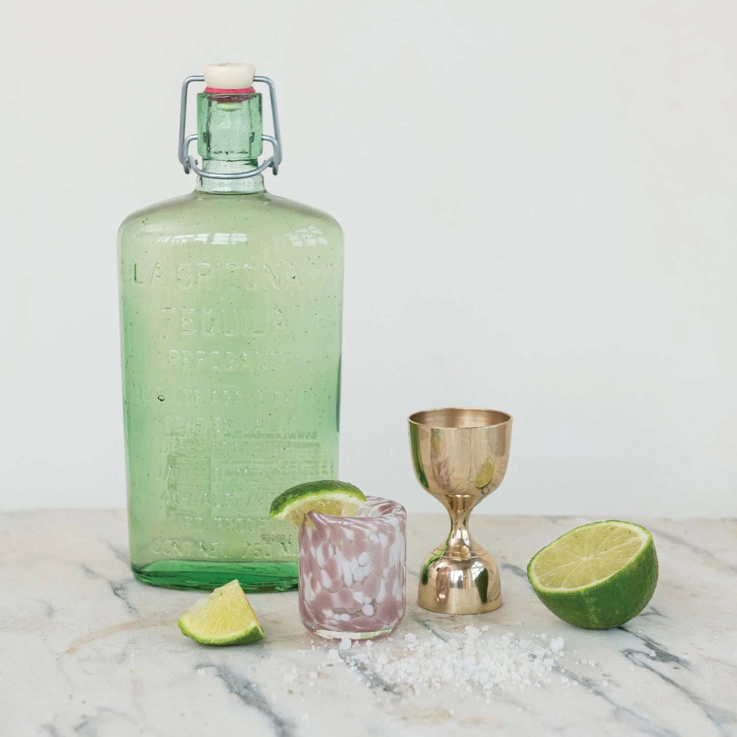 Green bottle with a gold and pink glass on a marble surface with limes.