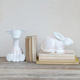 White ceramic giraffe and rabbit lamps on books against a plain wall