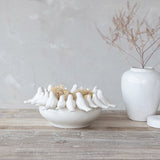 Decorative white bowl with bird sculptures and a vase on a wooden surface.