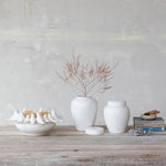White ceramic items including vases and bowls on a wooden surface with a light gray wall background.