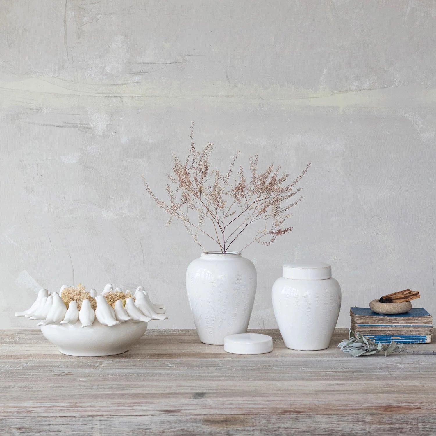 White ceramic items including vases and bowls on a wooden surface with a light gray wall background.