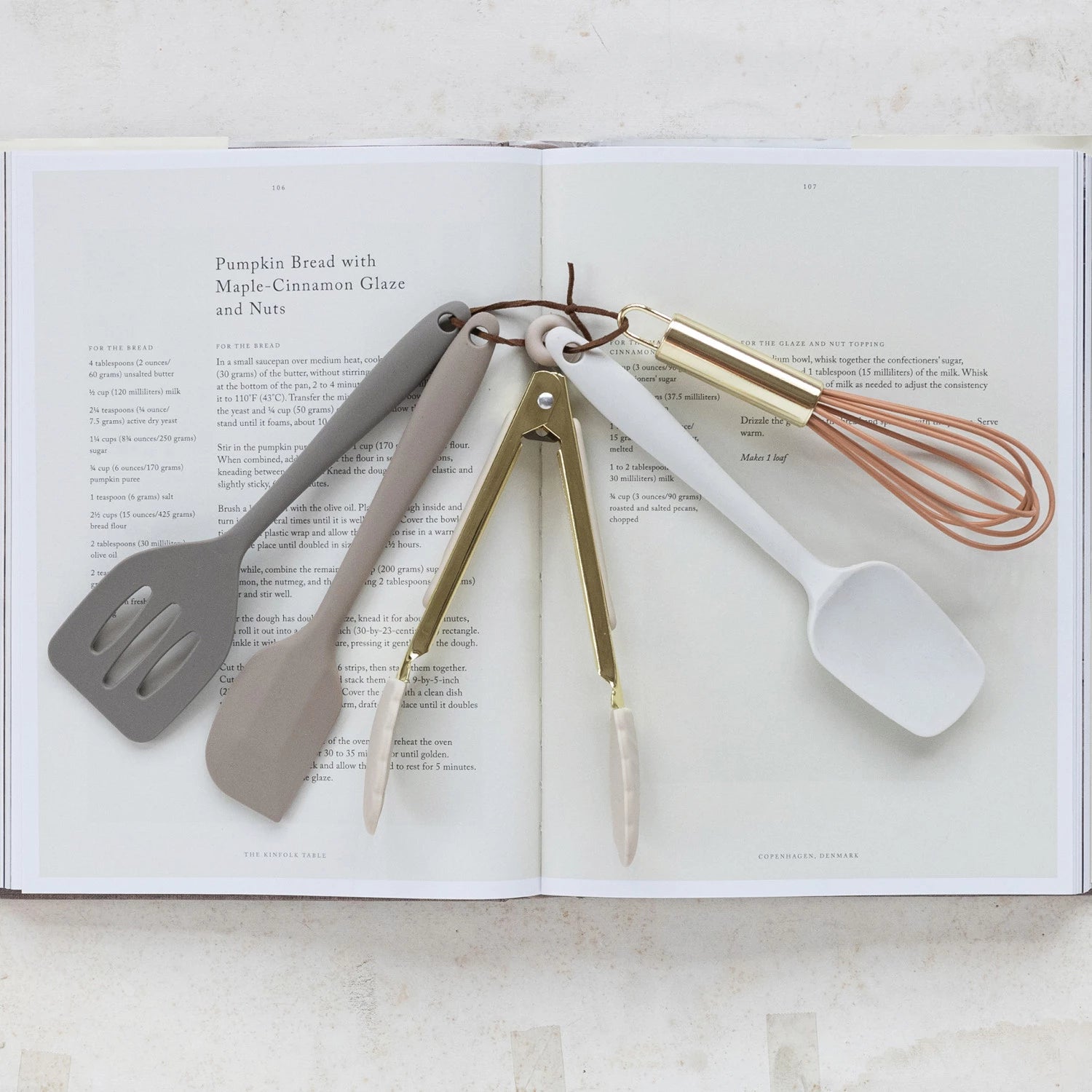 Set of kitchen utensils including a spatula, spoon, and whisk on an open book.
