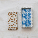 Two patterned napkin holders on a marble surface, one with brown spots and the other with blue floral design.