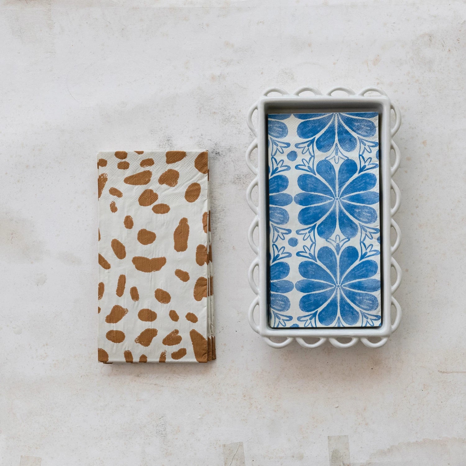 Two patterned napkin holders on a marble surface, one with brown spots and the other with blue floral design.