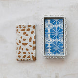 Two patterned napkin holders on a marble surface, one with brown spots and the other with blue floral design.